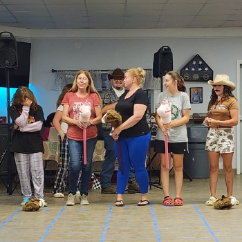 Various people in a line with stuffed horse heads on a stick, preparing to race.