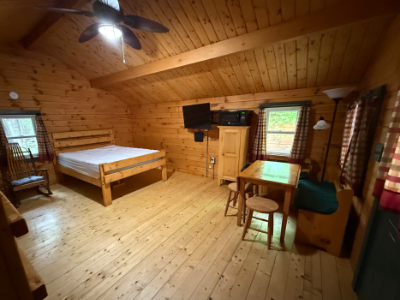 Picture of the inside of a cabin showin the queen sized bed, tv, and table.