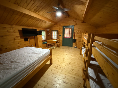 Picture of the inside of a cabin showin the queen sized bed, bunk beds, tv, table, and door.