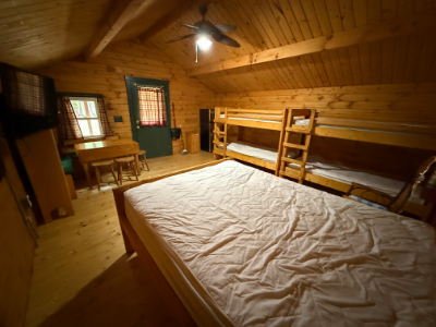 Picture of the inside of a cabin showin the queen sized bed, bunk beds, tv, table, and door.