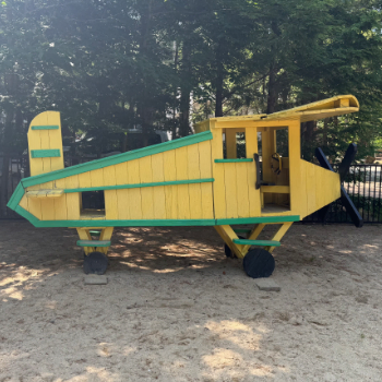 Wooden representation of an airplane painted yellow and green meant for children to play on.