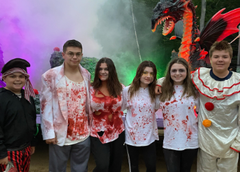 Children dressed up in halloween outfits with a dragon statue in the background.