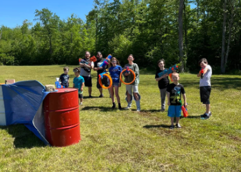 People in a field holding various nerf equipment and a red barrel in the foreground.