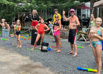 A group of people in bathing suites with water guns and balloons.